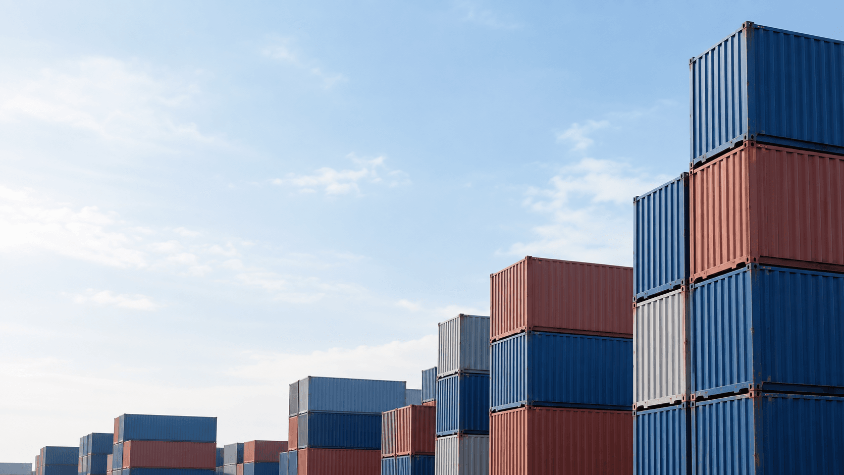 Stacks of blue and red freight containers in a bright international shipping yard